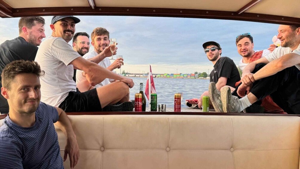 A group of people on a boat with a view of a river and a cityscape in the background. 1