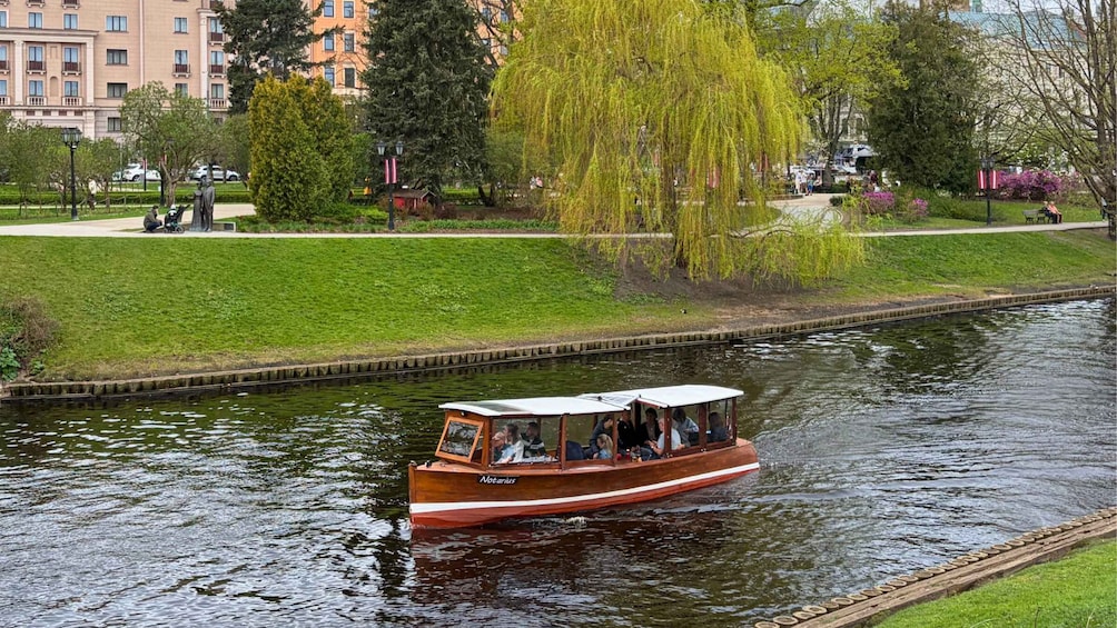 A wooden boat named 'Notarius' on a river, surrounded by greenery and buildings. 2