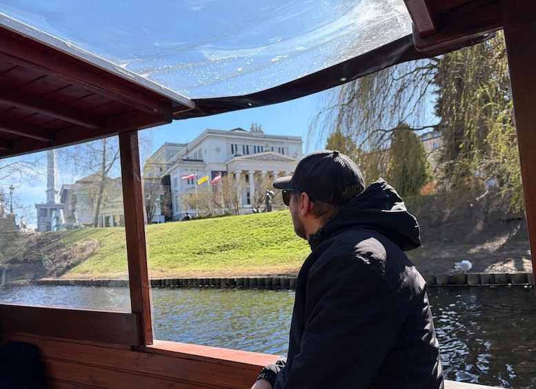 A person on a boat overlooking a river with a building and flags in the background. 3