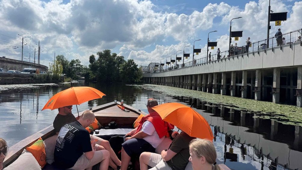 A group of people on a boat with orange umbrellas, a river, and a bridge with numbered signs. 2