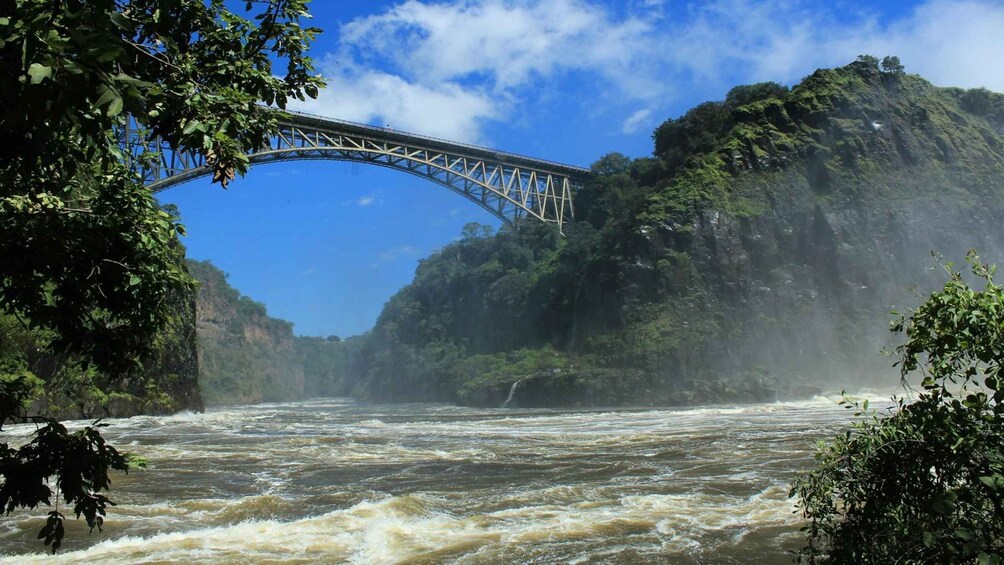 A river with a bridge, surrounded by lush greenery and a clear blue sky. 4