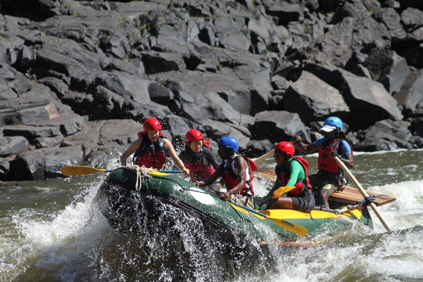 A group of people in a green and yellow raft navigating through a river with rocky banks. 1
