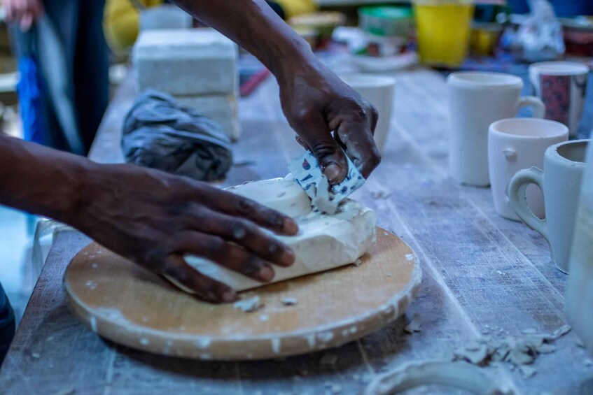 Hands shaping a clay object on a wooden board. 2
