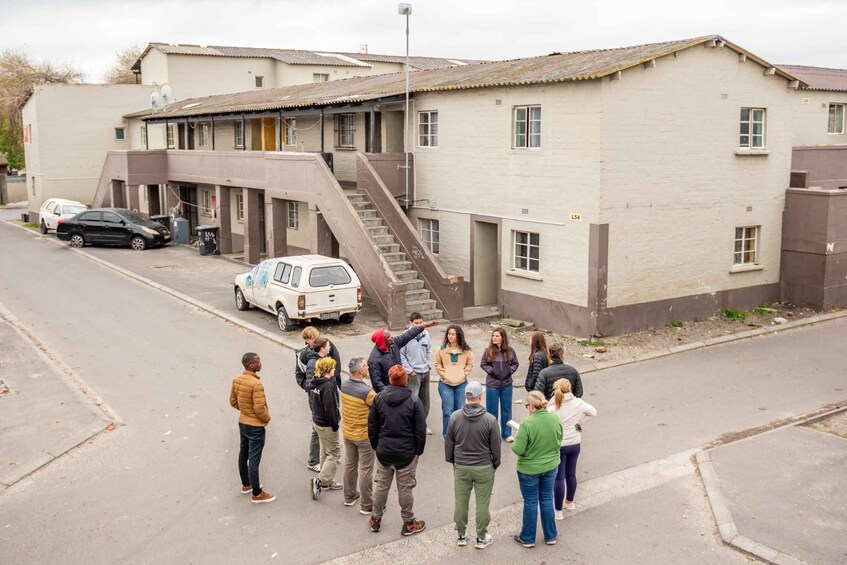 A group of people standing on a street in front of a building with a staircase leading to an upper level. 4