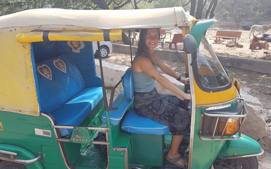 A woman sitting in a green and yellow auto-rickshaw with blue seats. 5