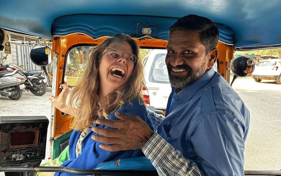 A man and a woman in an auto-rickshaw, with a motorcycle and a white car in the background. 3