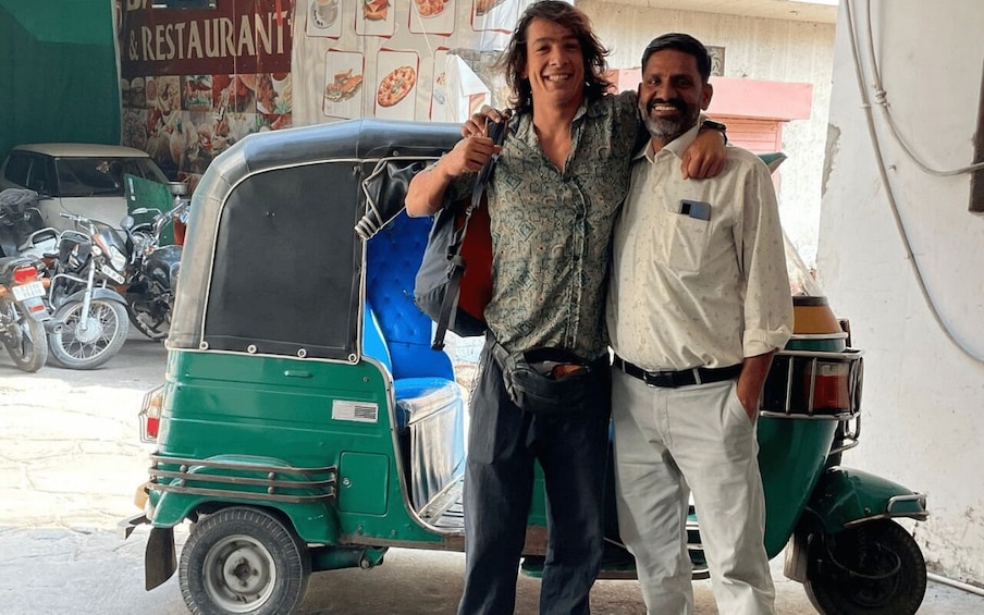 Two people standing next to a green auto-rickshaw with a blue interior, parked in front of a building with a sign that reads 'RESTAURANT'. 5