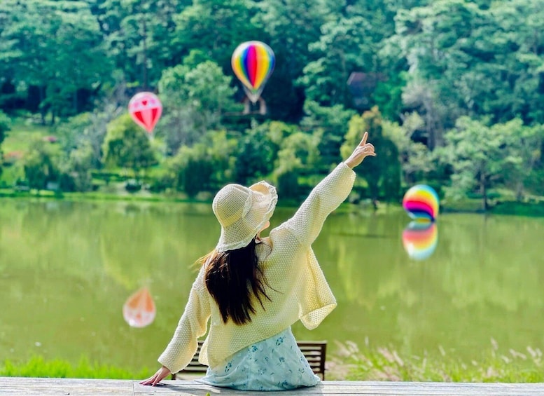 A person sitting by a lake with hot air balloons in the background. 1