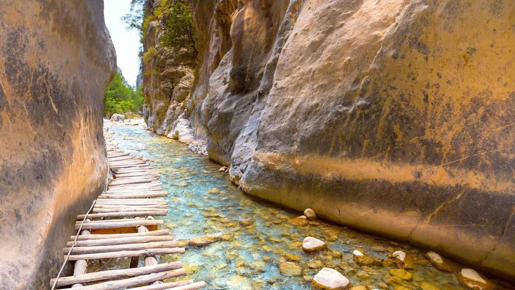 A narrow canyon with a wooden bridge over a clear stream. 1