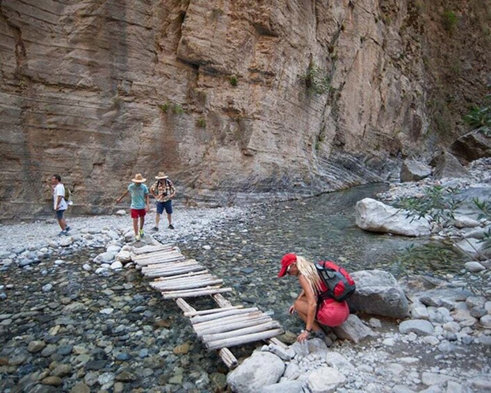 A group of people crossing a rocky stream on a wooden bridge. 2