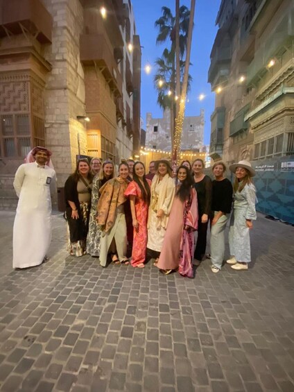 A group of people standing on a cobblestone street at dusk, with buildings and palm trees in the background. 5