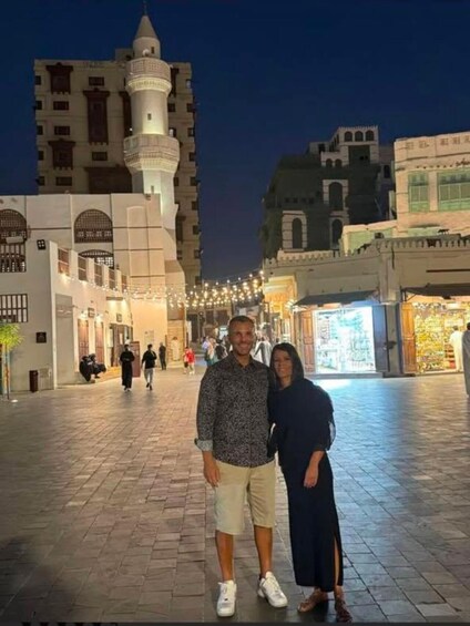 A couple posing in a historic square with a prominent tower and traditional architecture. 2