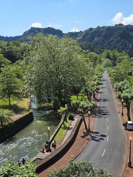 A river running alongside a road with trees and lamp posts, with mountains in the background. 3