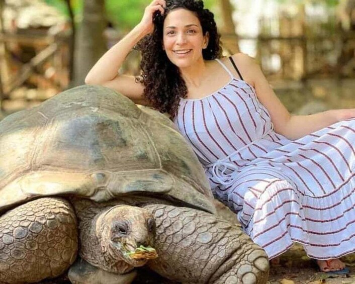 A person sitting next to a large tortoise in a natural setting. 1