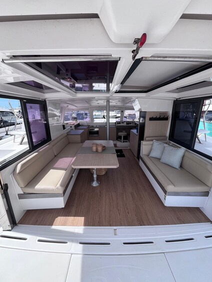 A boat interior with a central table, cushioned seating, and a kitchen area. 3