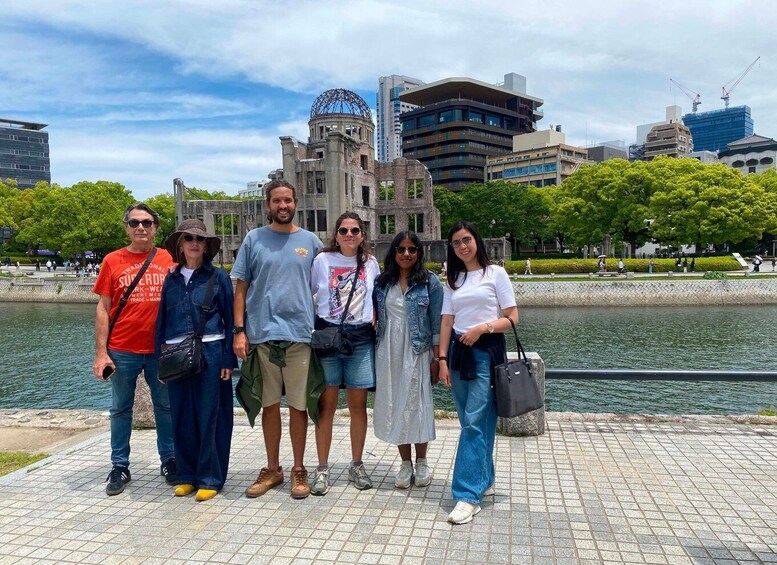 A group of people standing by a waterfront with modern buildings and a historic structure in the background. 2