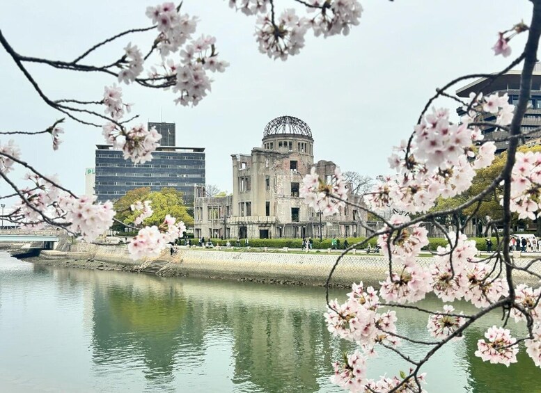 A river with cherry blossoms in the foreground, a historic building with a dome, and modern skyscrapers in the background. 1