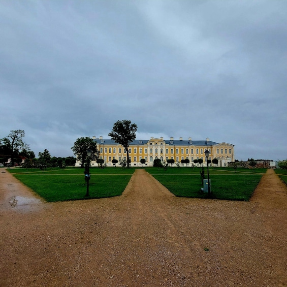 A large yellow building with a symmetrical facade, surrounded by a well-maintained lawn and a gravel path leading to it. 2