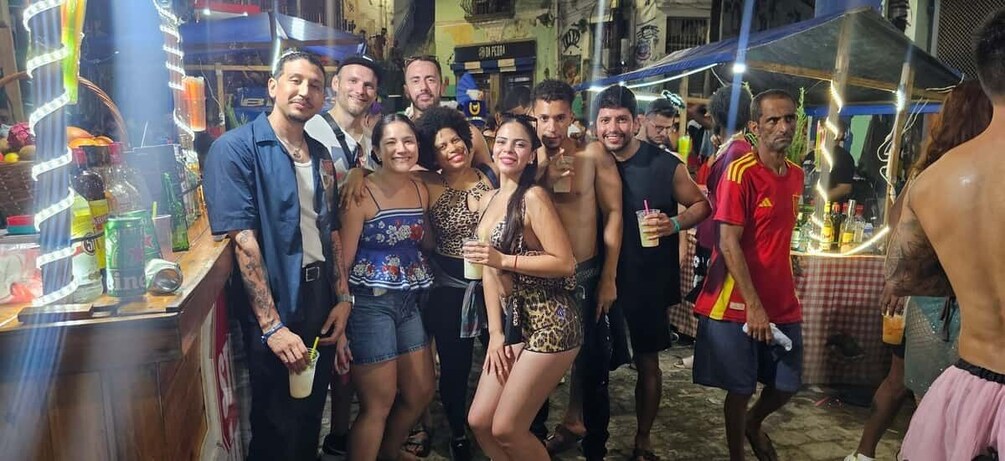 A group of people gathered around a bar area with bottles and drinks. 1