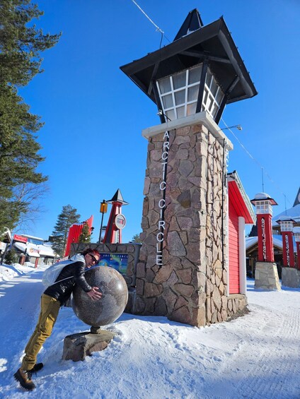 Une tour de pierre sur laquelle est inscrit « Cercle arctique », entourée de neige et d’arbres. 3