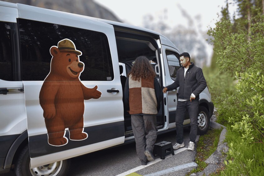 A white van with a bear sticker on the side parked on a road with greenery on the side. 4