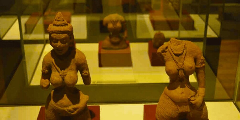 Three ancient sculptures in a museum display case. 2