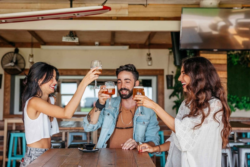 Three people toasting with drinks at a wooden table in a casual dining setting. 3