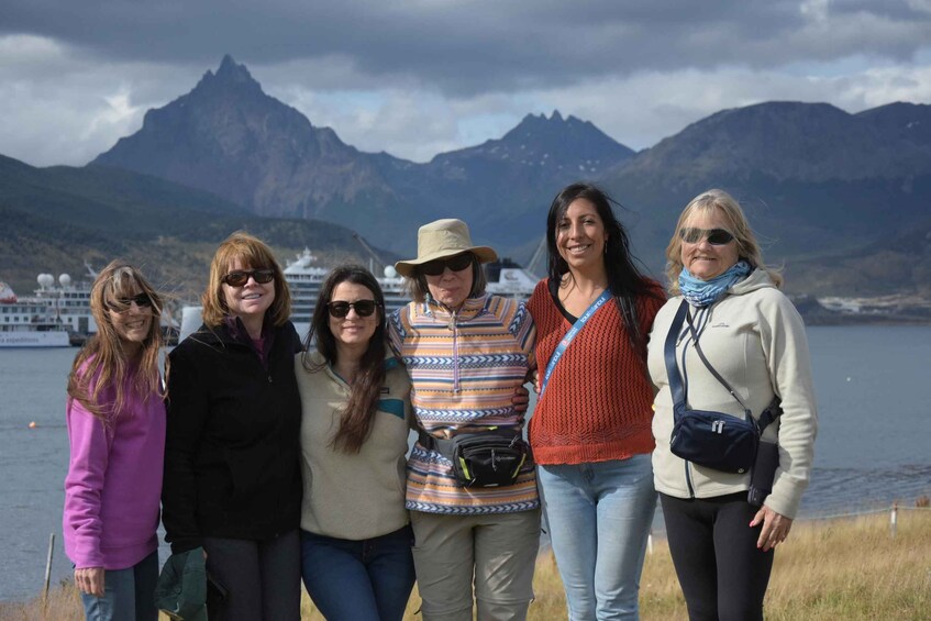 A group of people standing by a body of water with mountains in the background. 2