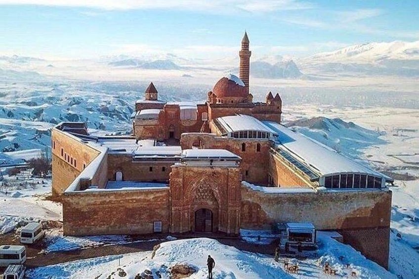 A snow-covered fortress with a prominent minaret and a large central building. 1