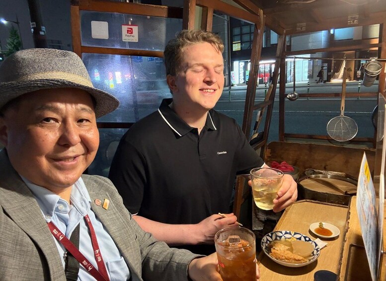 Two people at a food stall with drinks and a plate of food. 3
