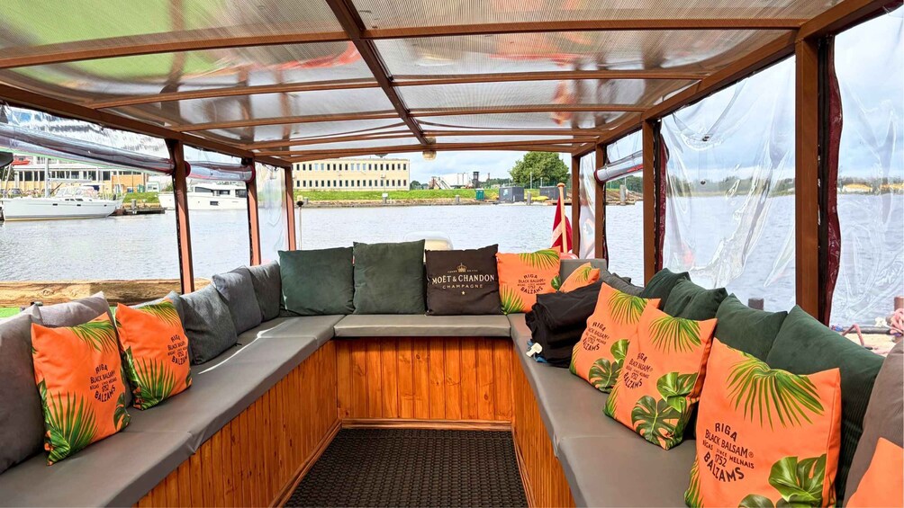 A boat interior with a covered seating area, wooden paneling, and a view of the water and buildings. 2