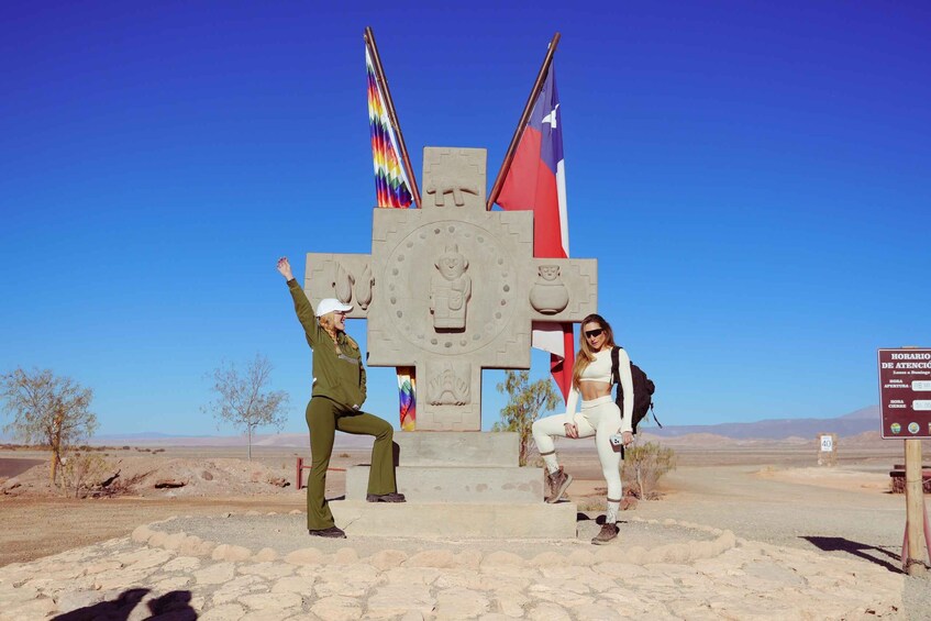 Two people posing in front of a large stone monument with flags, in a desert landscape. 2