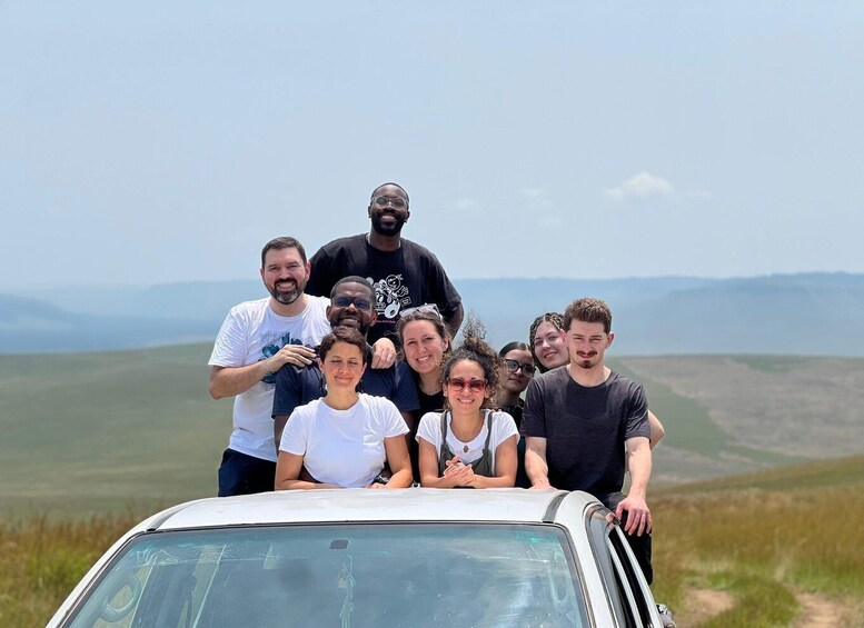 A group of people posing in front of a white car on a grassy field with a clear sky. 1