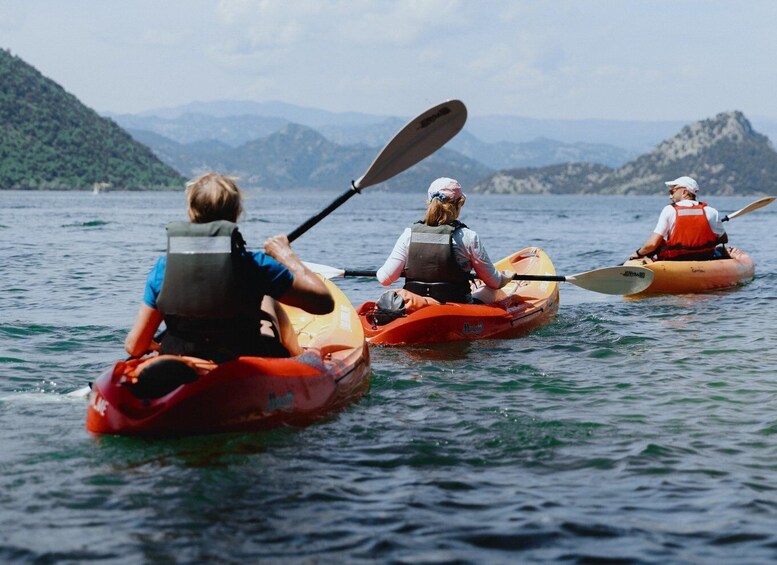 Three people kayaking on a lake with mountains in the background. 1