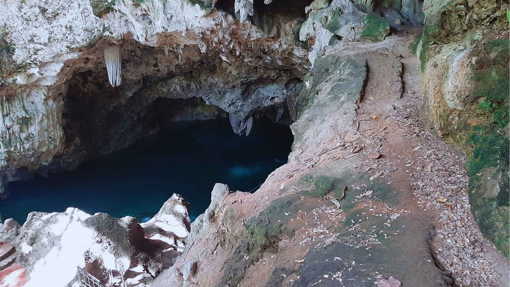 A rocky cave entrance with a narrow path leading into a dark blue pool. 2