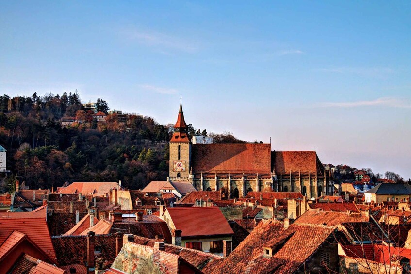 A town with red-roofed buildings, a prominent church with a tall tower, and a hillside in the background. 3