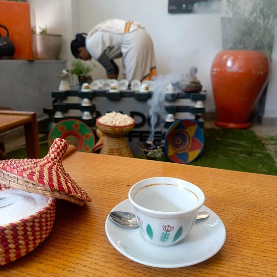 A cup of coffee on a table with a spoon, surrounded by colorful bowls and a woven basket. 5