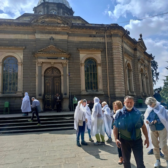 A group of people standing in front of a historic building with large arched windows and a dome. 1