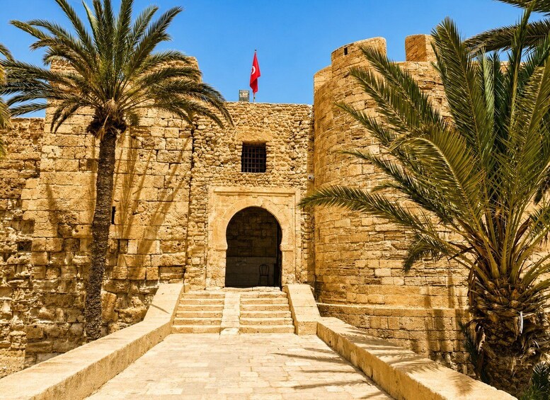A stone fortress with a flag, palm trees, and a staircase leading to an entrance. 4