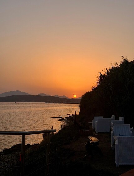 A sunset over a body of water with chairs and a fence. 5