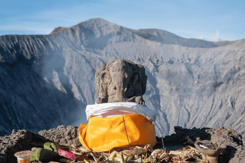 A stone statue on a mountain with a yellow cloth and incense sticks. 5