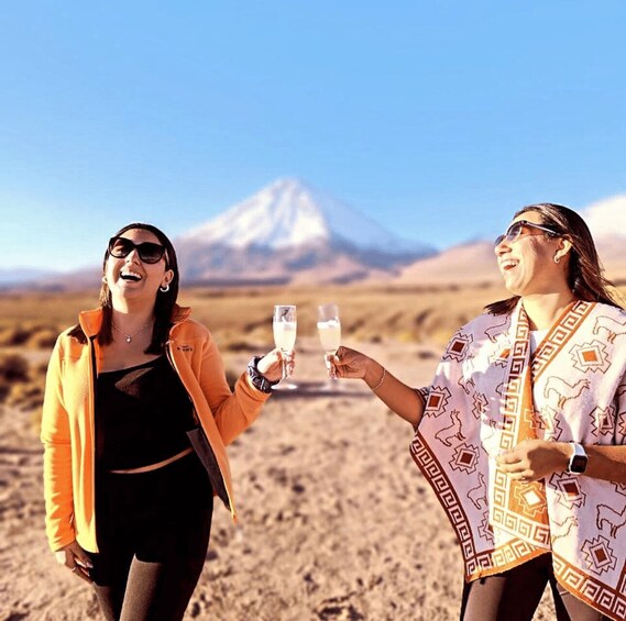 Dos personas brindando con copas de champán en un paisaje desértico con una montaña al fondo. 5