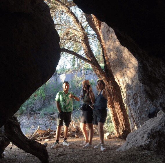 Tres personas en una cueva con formaciones rocosas naturales y vegetación escasa. 3