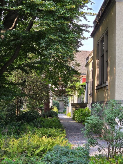 A garden path leading to a building with a tiled roof, surrounded by lush greenery and trees. 2