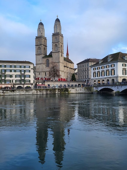 A historic cathedral with twin towers and a red spire, reflecting in a calm river. 1