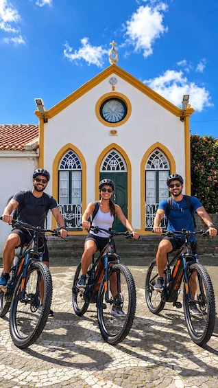Three people on bicycles in front of a building with a clock and arched windows. 1
