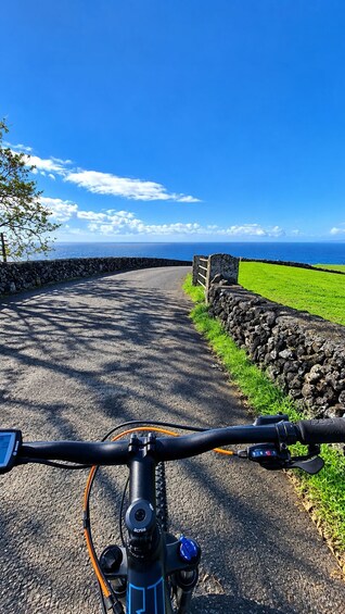 A bicycle on a paved road with a stone wall and grassy area on one side, and a clear blue sky above. 2