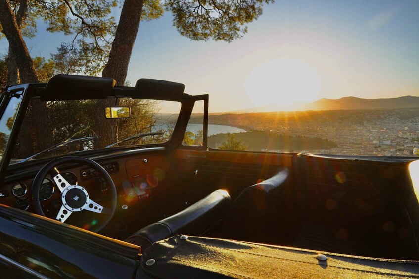 A convertible car's interior with a steering wheel and dashboard, and a scenic view of a city and mountains in the background. 4
