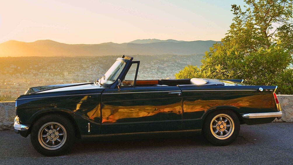 A black convertible car parked on a road with a cityscape and mountains in the background. 2