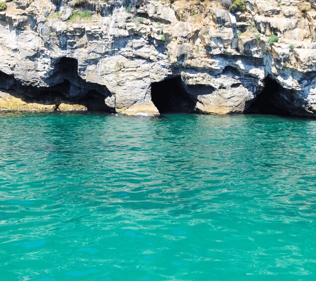 A coastal rock formation with two large caves in turquoise water. 2